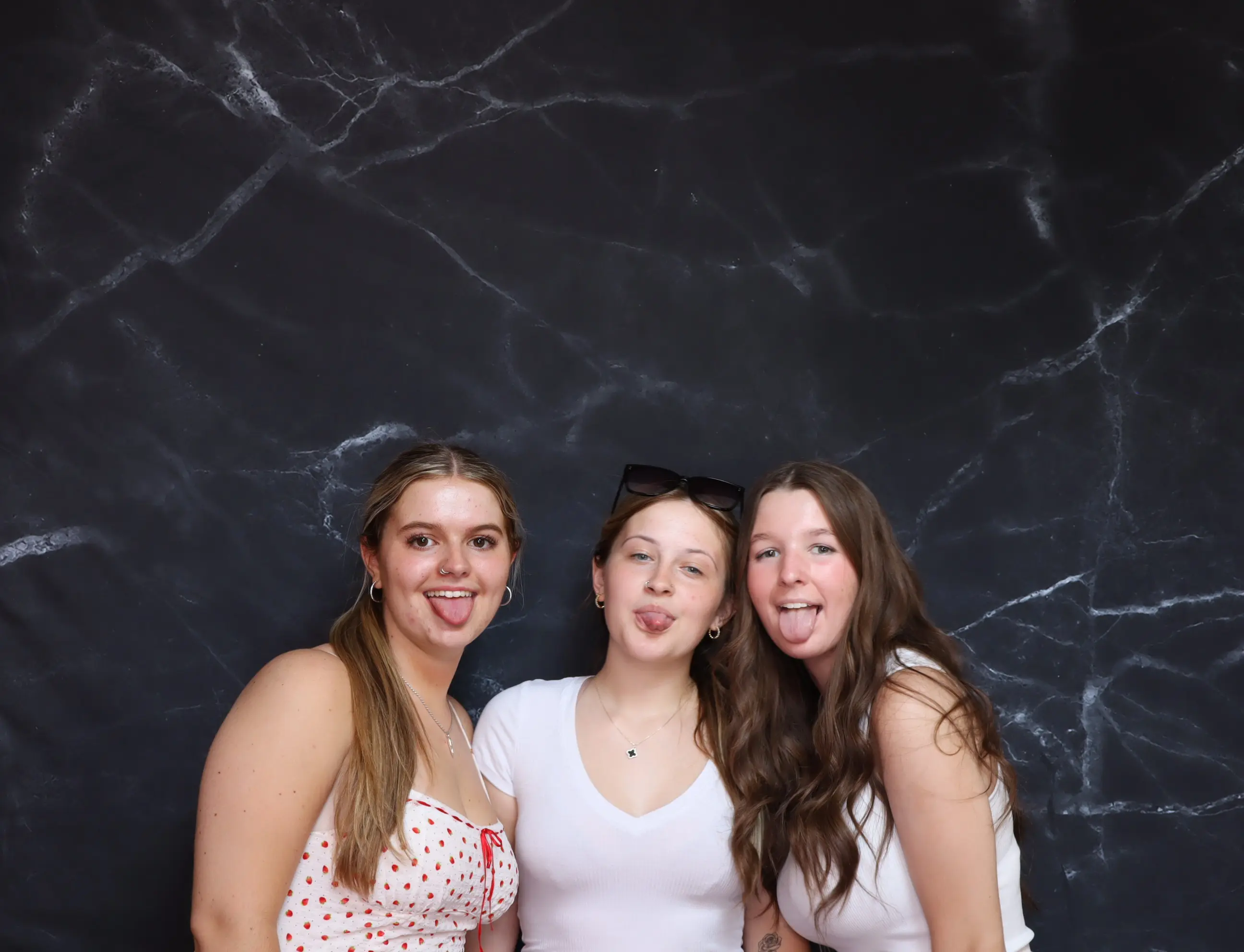 Three young women posing happily against a dark textured background.