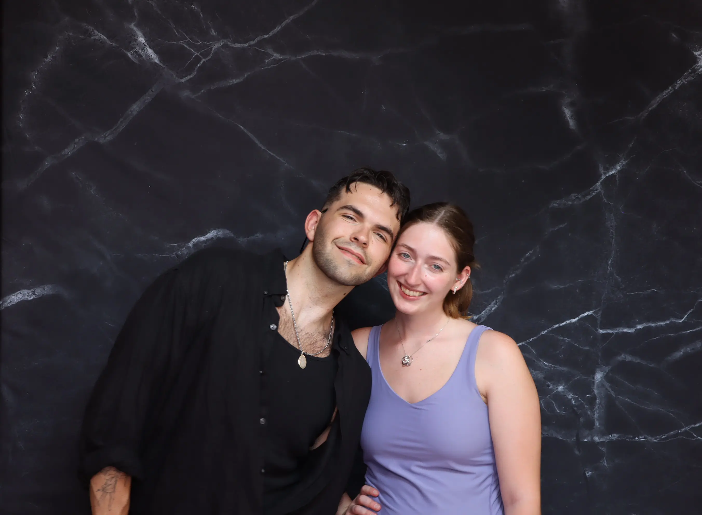 A smiling couple poses against a dark marbled background.