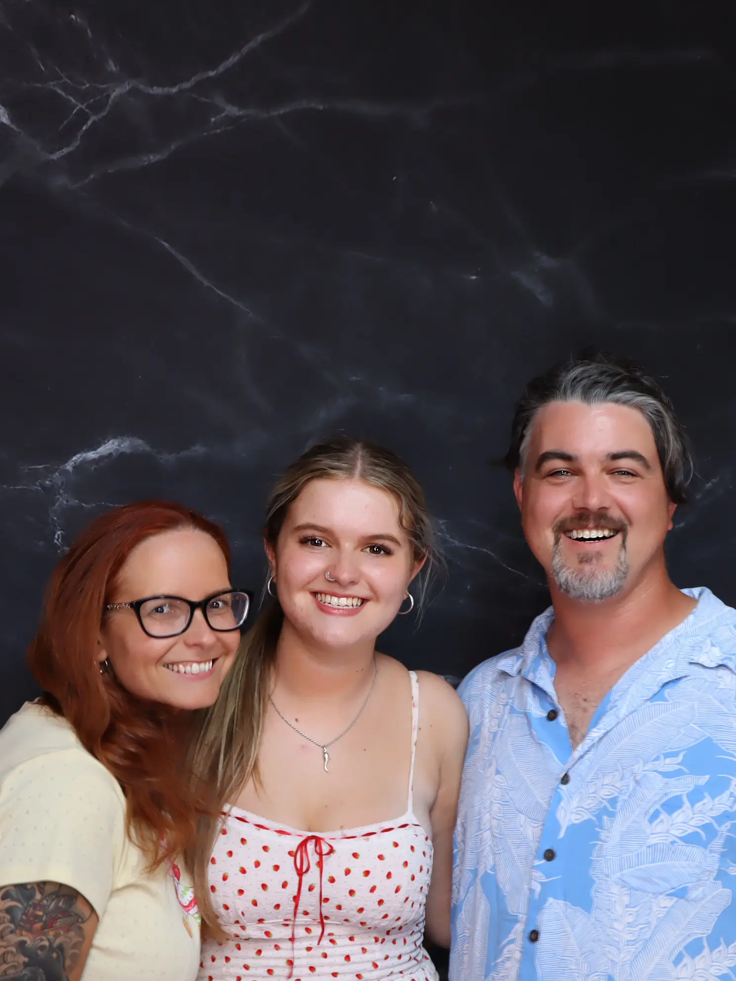 Three people smiling together against a dark background.