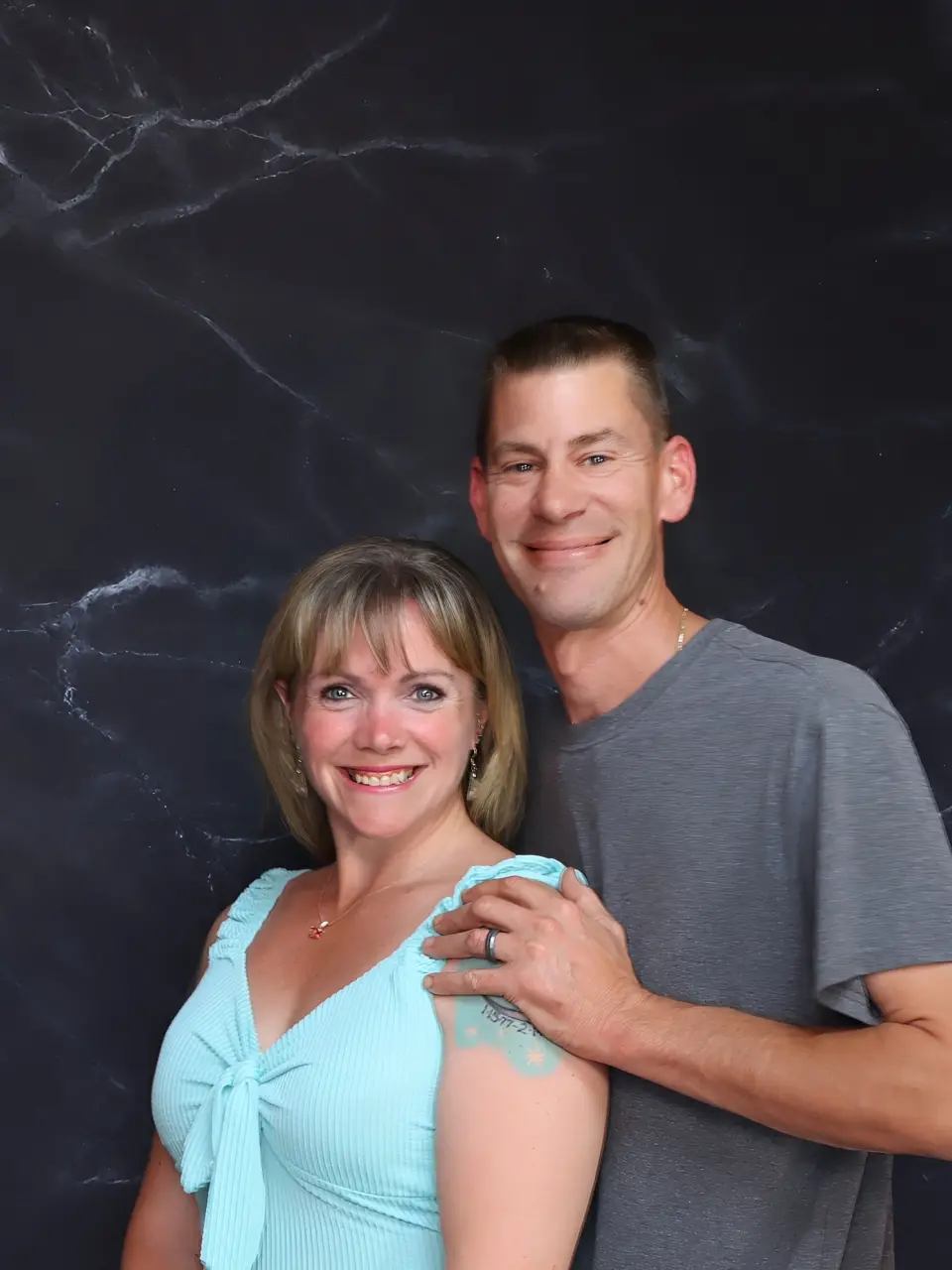 Smiling couple posing against a dark marble background.