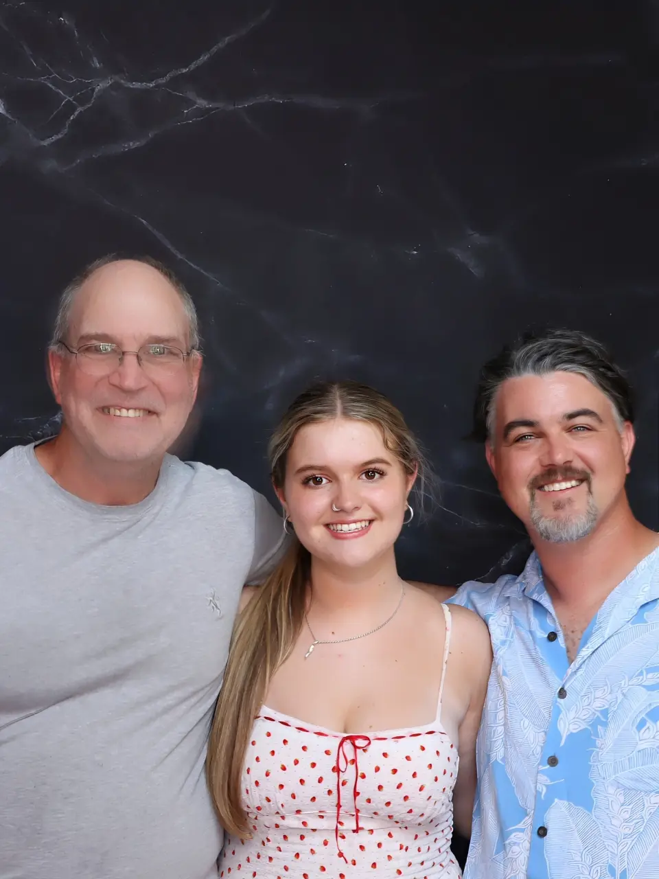 Three smiling people posing together indoors against a dark background.