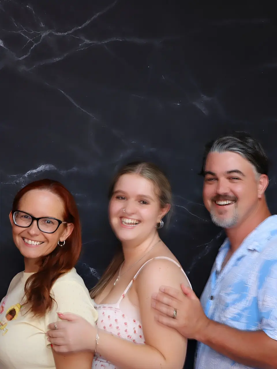 Three friends smiling together against a dark background.