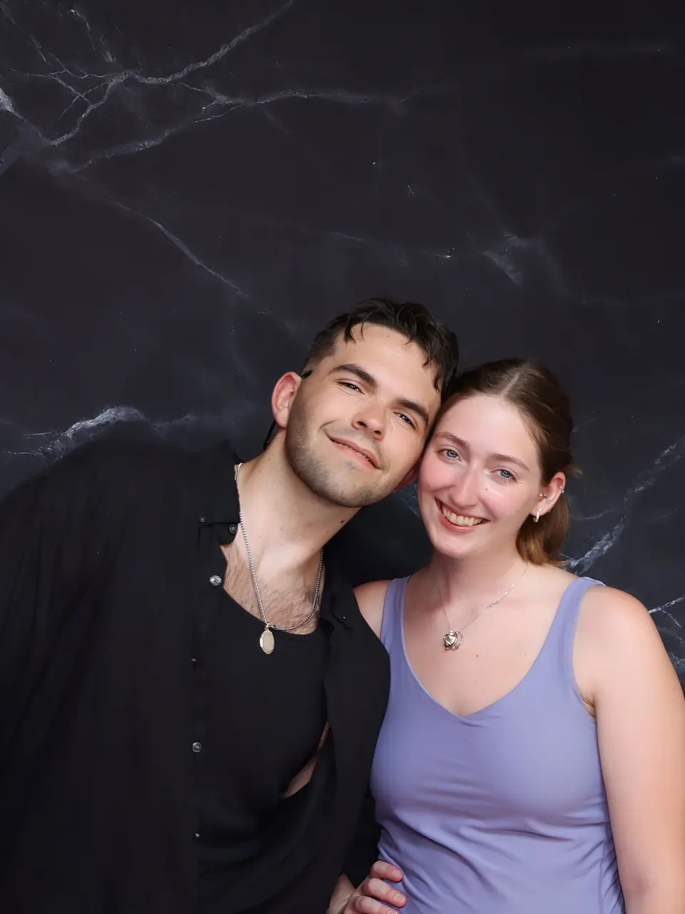 A happy young couple posing against a dark backdrop.