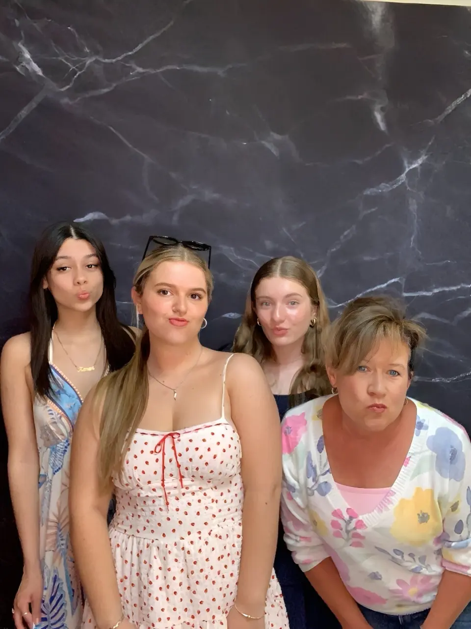 Four young women posing against a dark marbled background.